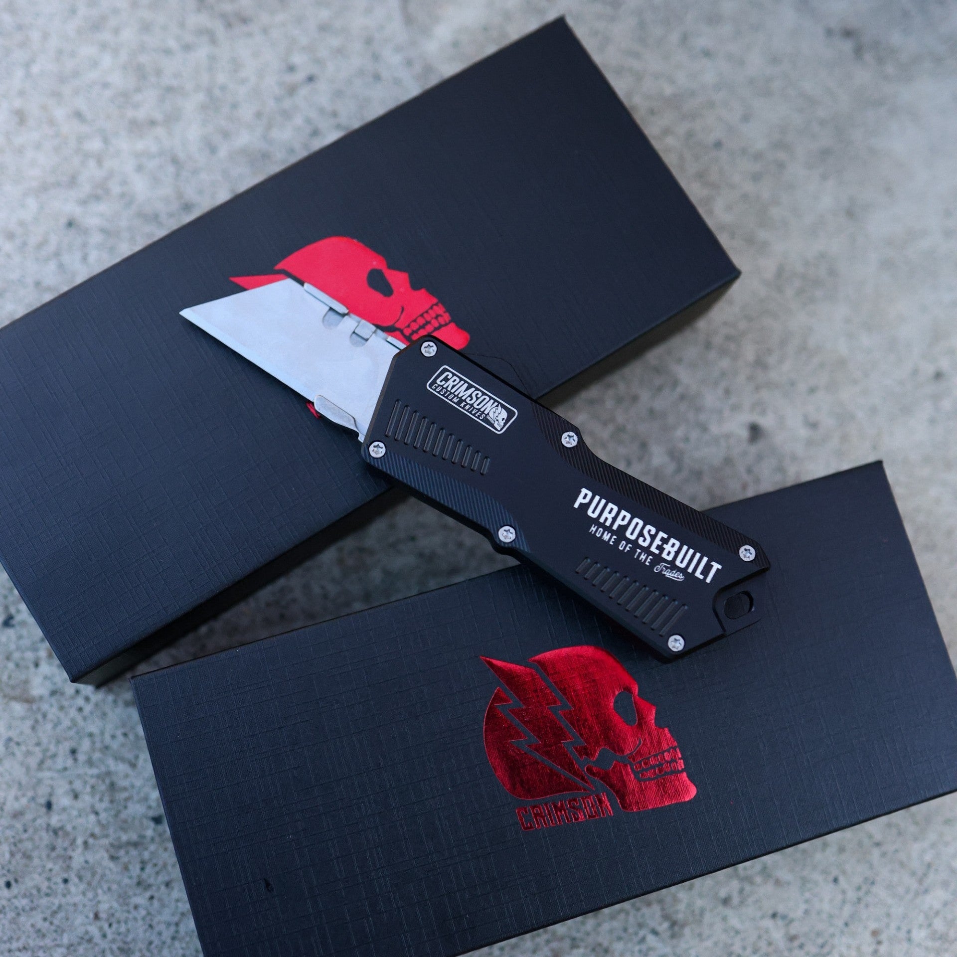 Knife with 'Pursue Built' branding on a black box with red logo on a concrete surface