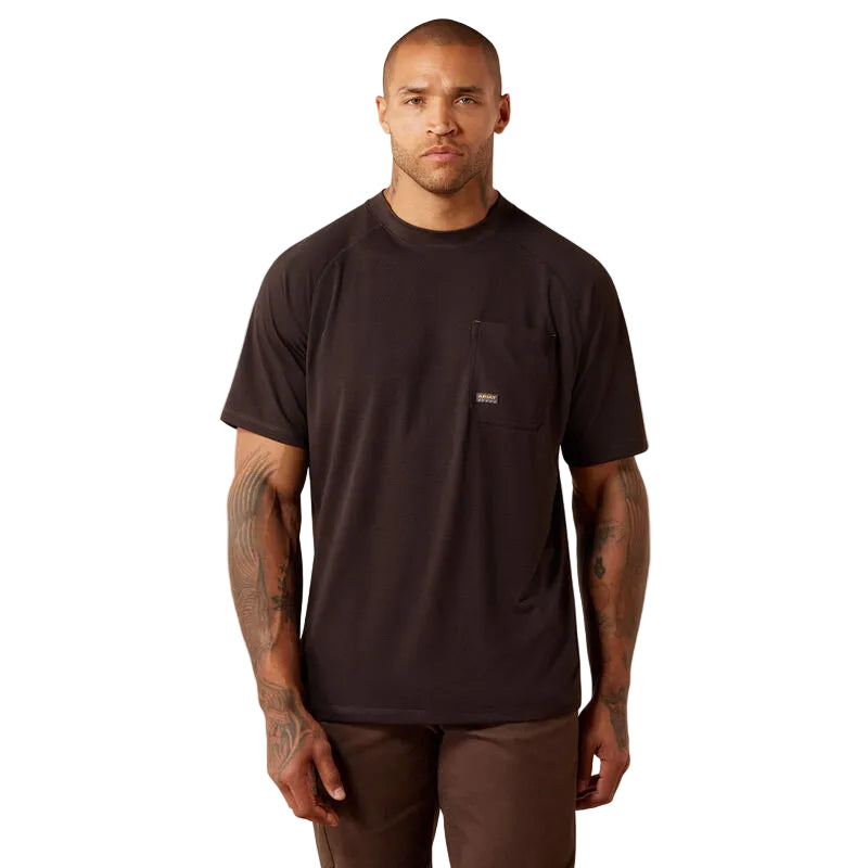 A man wearing a dark brown short-sleeve crewneck t-shirt with a chest pocket, paired with brown pants, standing against a light beige studio background.