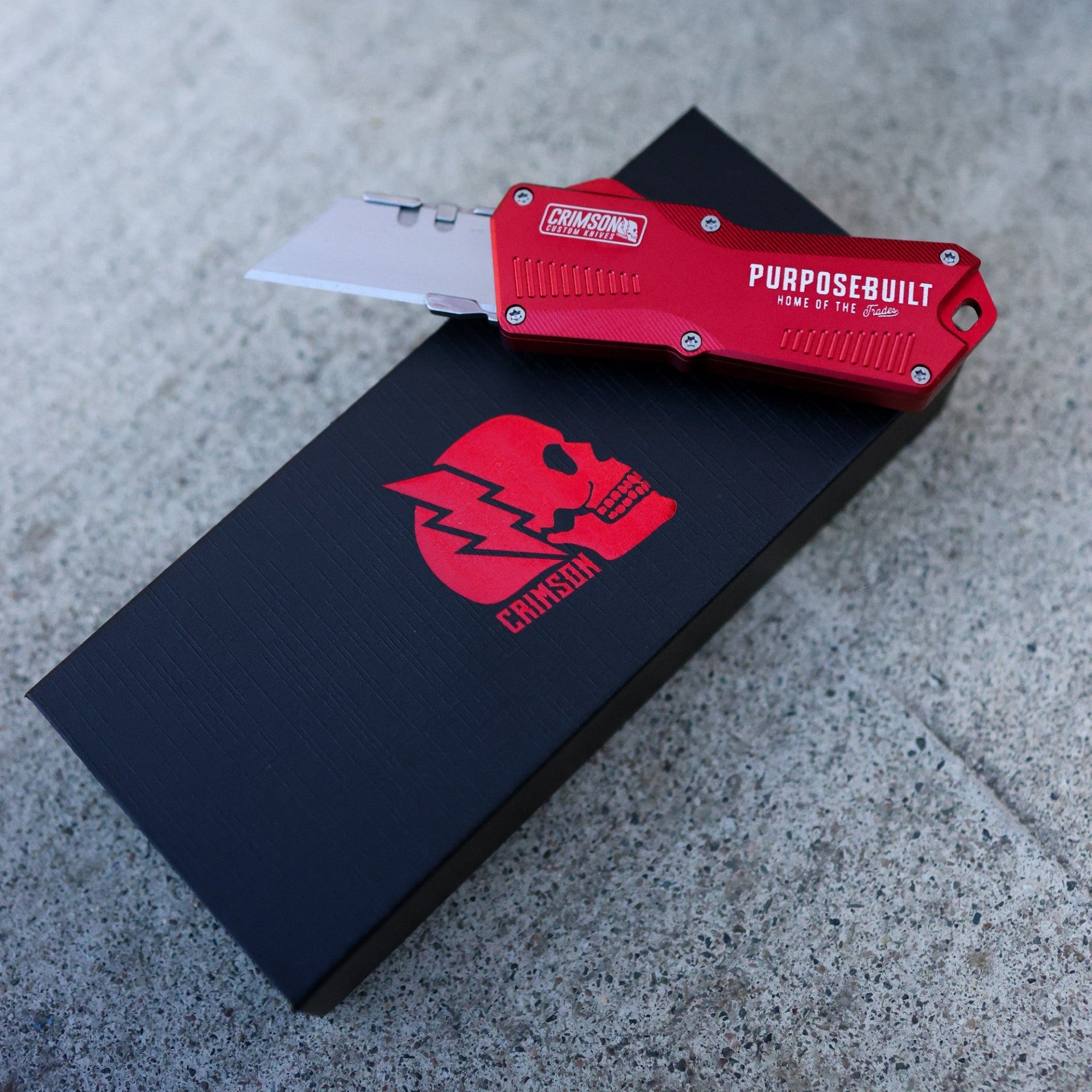 Red pocket knife on a black surface with a logo, on a concrete floor.