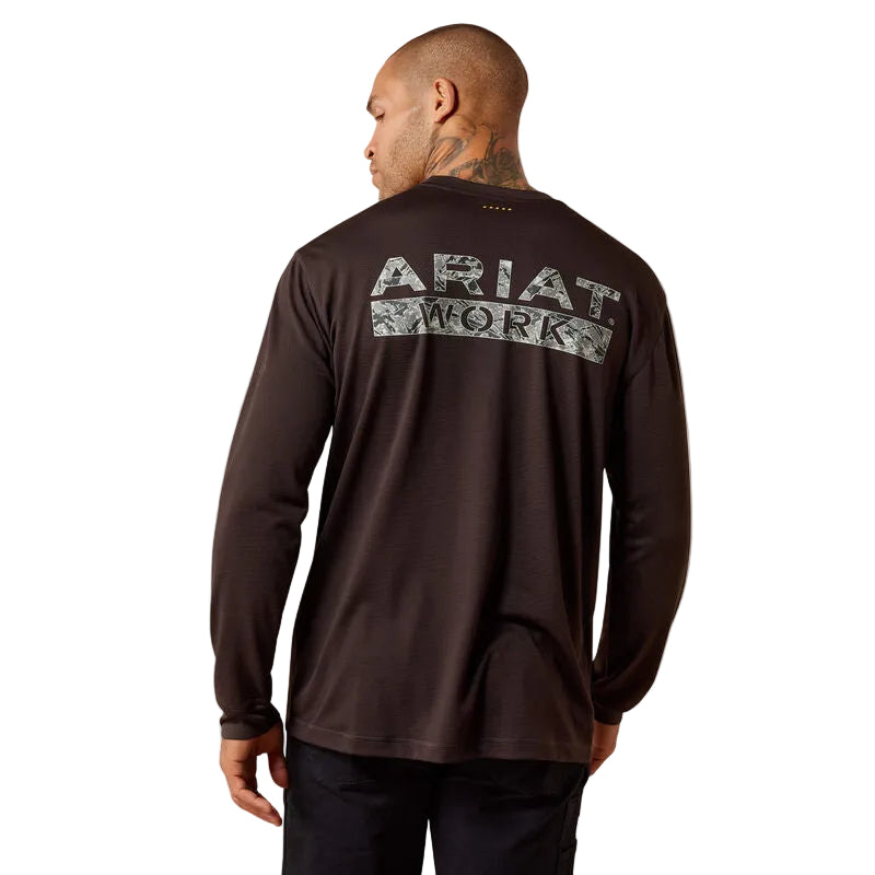 A man viewed from the back wearing a dark brown long-sleeve performance shirt with a large 'ARIAT WORK' logo printed across the upper back in a distressed gray and white pattern.
